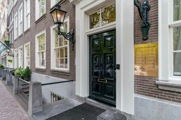 Ingang van een statig pand aan Lange Voorhout 86 met donkere voordeur, gevelverlichting en bedrijfsnaamplaat.